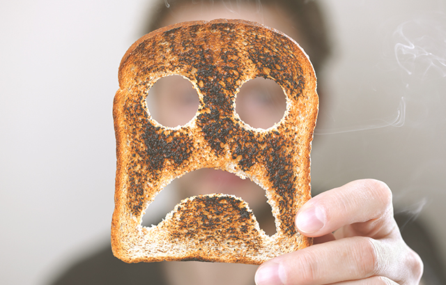 悲しい顔の形にくりぬかれた焦げたトーストを持つ男性
