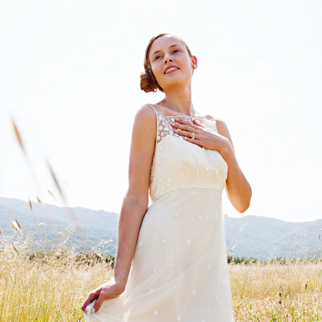 ウェディングドレスを着た女性が胸に手を当て草原の中に立っている様子