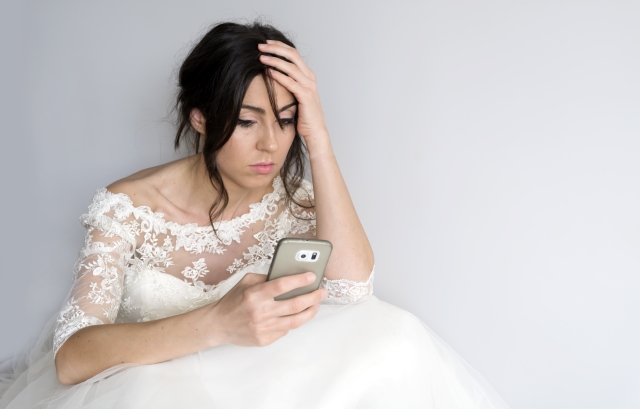 スマホを見ながら頭を抱えるウェディングドレス姿の女性