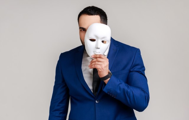 仮面を持ったスーツ姿の男性