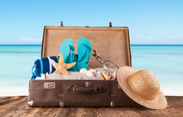 海の前に置かれたスーツケース、麦わら帽子、ビーチサンダル