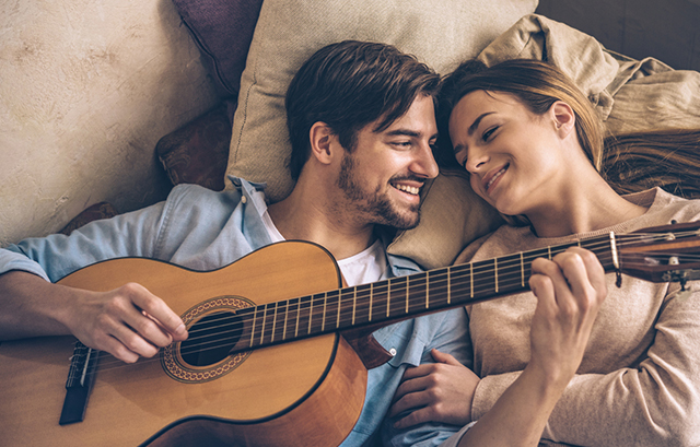 笑顔でギターを弾く男性と寄り添って聴いている女性