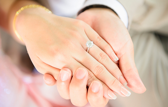 婚約指輪をした女性の手を男性の手が下から支えている様子