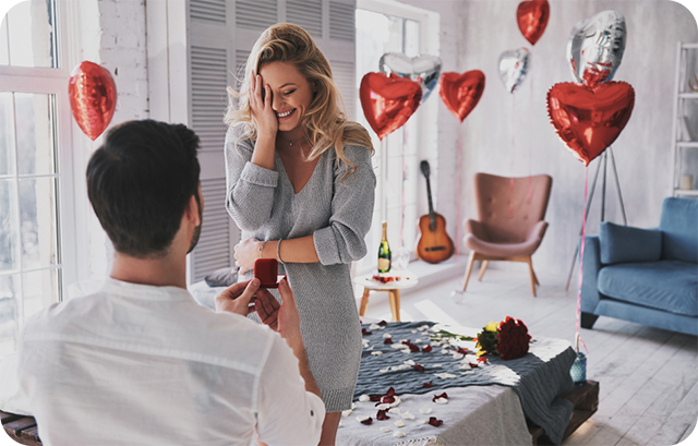 風船と花で飾られた部屋でプロポーズする男性と喜んでいる女性