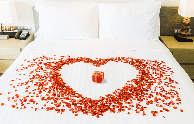 ベッドに赤い花びらで描かれたハートと、その中央に置かれた小さな赤い箱