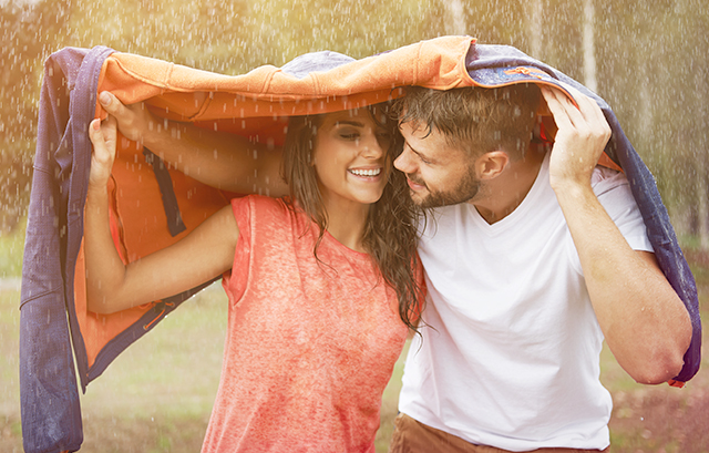 パーカーを傘替わりに雨を凌ぐ笑顔の男女