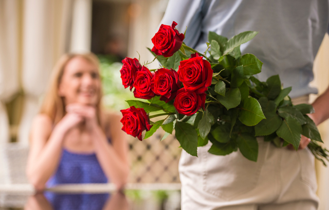 女性の前で背中に赤いバラの花束を隠している男性