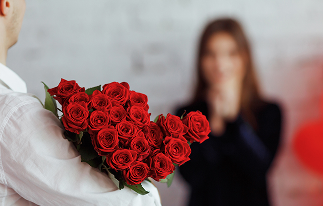 バラの花束を抱えている男性とその奥で感激している女性