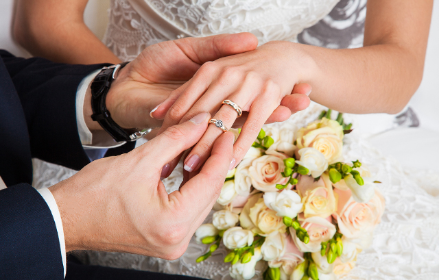 新婦が付けている結婚指輪の上から婚約指輪を嵌める新郎