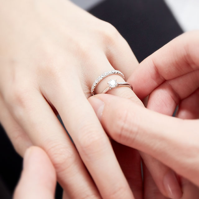 結婚指輪をつけた指に上から婚約指輪をつける様子