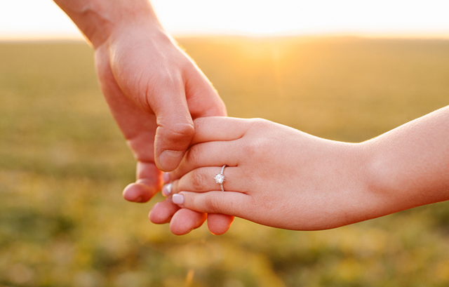 左手薬指に婚約指輪を嵌めた女性と手を繋ぐ男性
