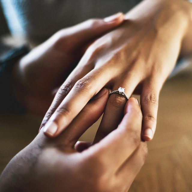 女性の指に婚約指輪をはめている男性