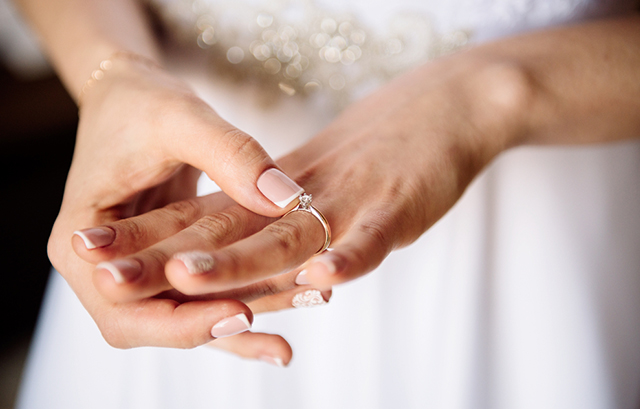 自分の薬指の婚約指輪を触る女性の手元