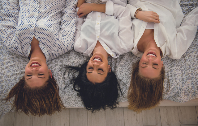 布団に並んで寝転がって笑っている3人の女性