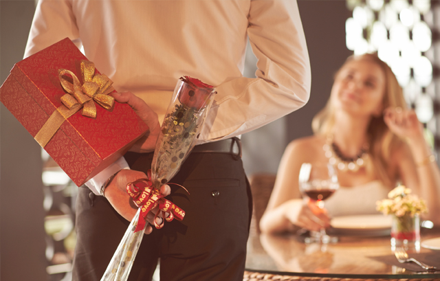 体の後ろにプレゼントとバラの花を隠している男性