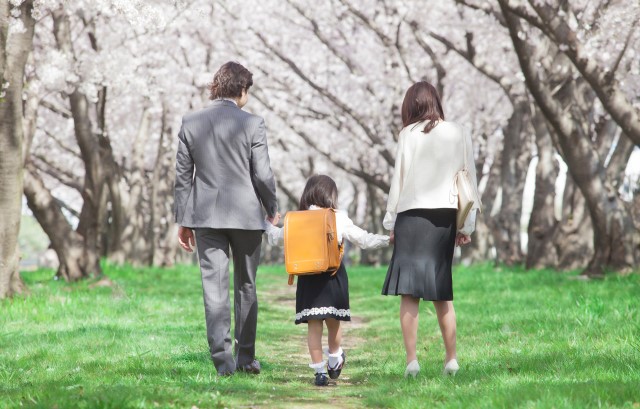桜の下を両親と小学生が歩く様子