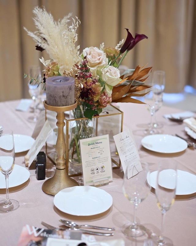 薄ピンクのテーブルクロスに、落ち着いたカラーリングの装花が飾られたゲストテーブル。