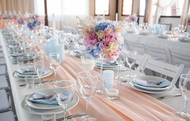 パステルピンクのランナーがかけられた長テーブルに、淡いブルーのナプキンやキャンドルが装飾された様子