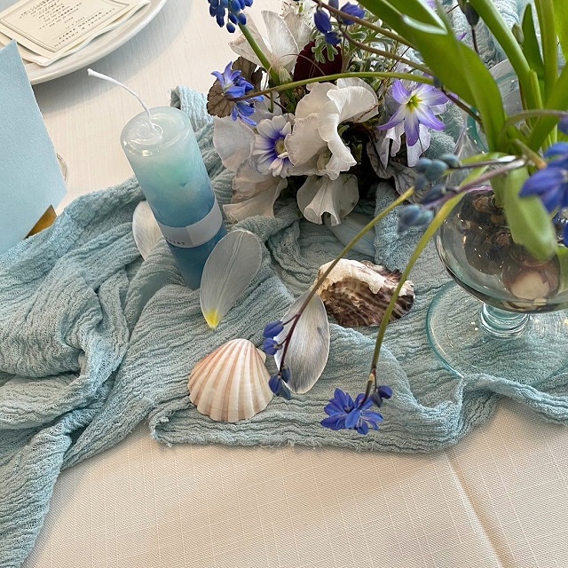 くすみブルーの布の上に貝殻や花が飾られている