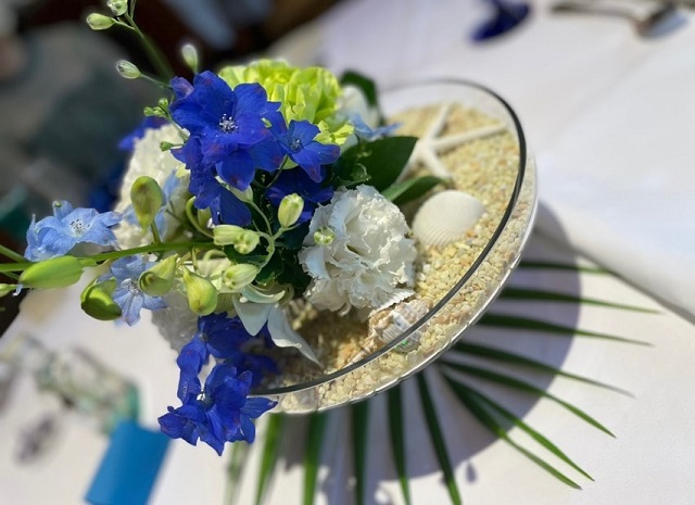 平たい容器に砂、貝、ヒトデ、それに花が飾り付けられたもの