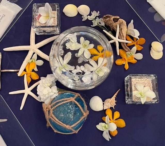 紺色に近い青のテーブルクロスに、オレンジ色の花や貝殻、ヒトデなどが飾られている