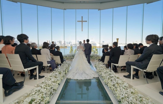 海が見えるロケーションのチャペルでガラスのバージンロードを歩く新郎新婦