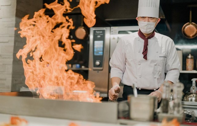 オープンキッチンで豪快に調理するシェフ