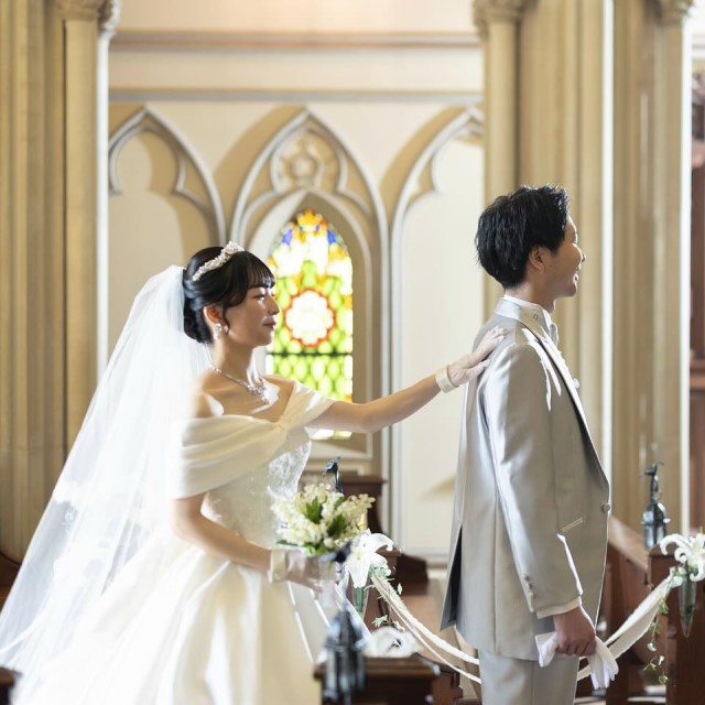 後ろを向いた新郎の肩を叩くドレス姿の新婦