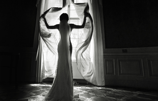 カーテンを開ける花嫁の白黒写真