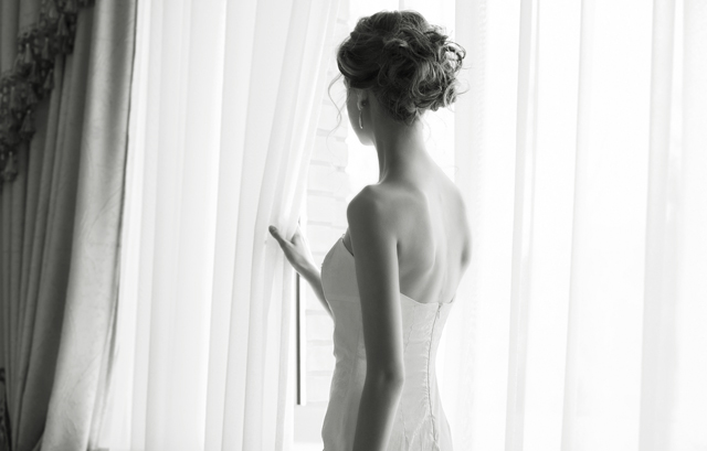 斜めを向いてカーテンに触れる花嫁の白黒写真