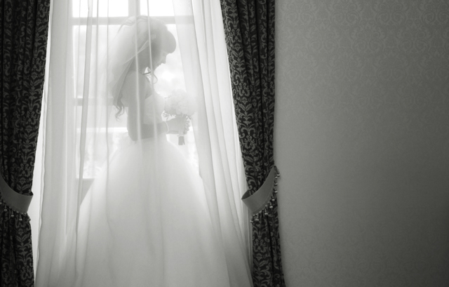 カーテンの中に入った花嫁の白黒写真