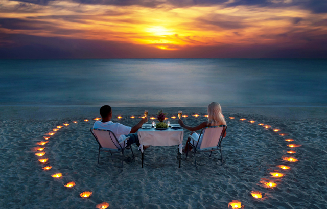 砂浜にキャンドルを並べて中心に座るカップル