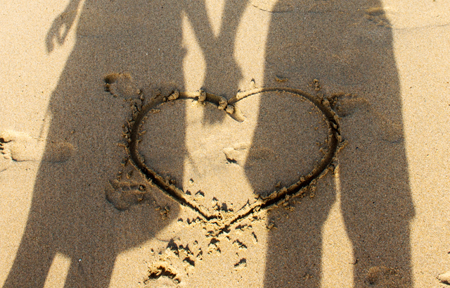 砂浜に描かれたハートと手をつなぐカップルのシルエット