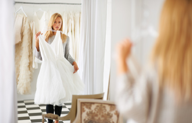 ウェディングドレスを体に合わせて鏡で確認する女性