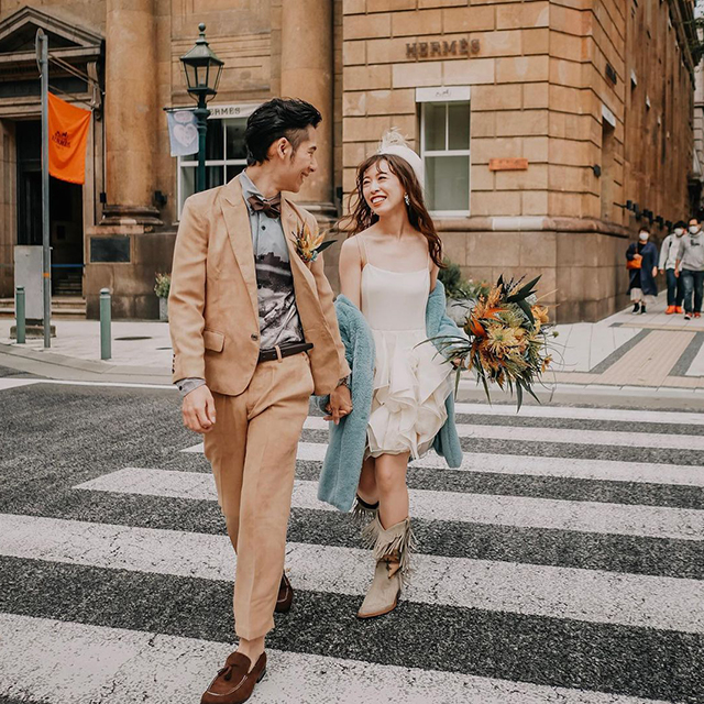 横断歩道を笑顔で渡る新郎とミニ丈ウェディングドレスの新婦
