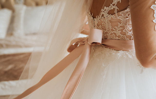 ウェディングドレスに淡いピンクのサッシュベルトを巻いた花嫁