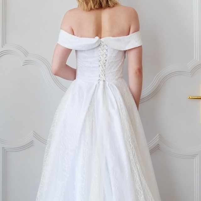 ウェストを編み上げで留めた、オフショルダーのドレスを着た花嫁