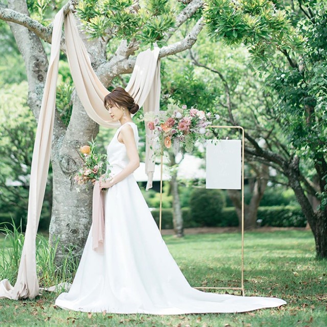 ガーデンに立つ、ゆるめのシニヨンとロングトレーンドレスをコーディネートした花嫁