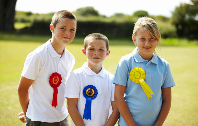 それぞれ異なる色のロゼットをつけた3人の子供
