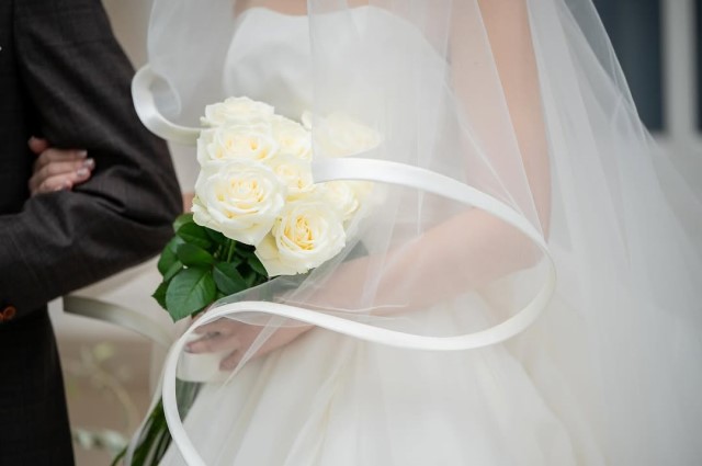 白いバラの花束を抱えてベールをつけた花嫁