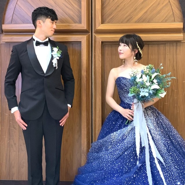 黒いタキシードを着た新郎と青いカラードレス姿の新婦
