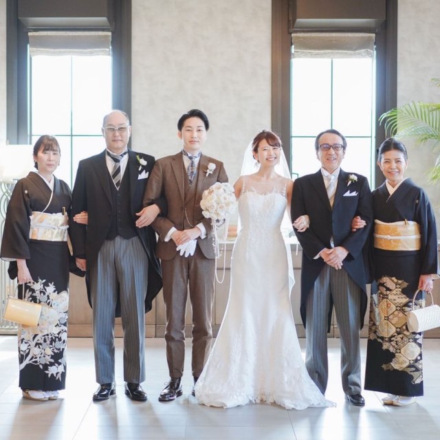親と並んで腕を組む新郎新婦