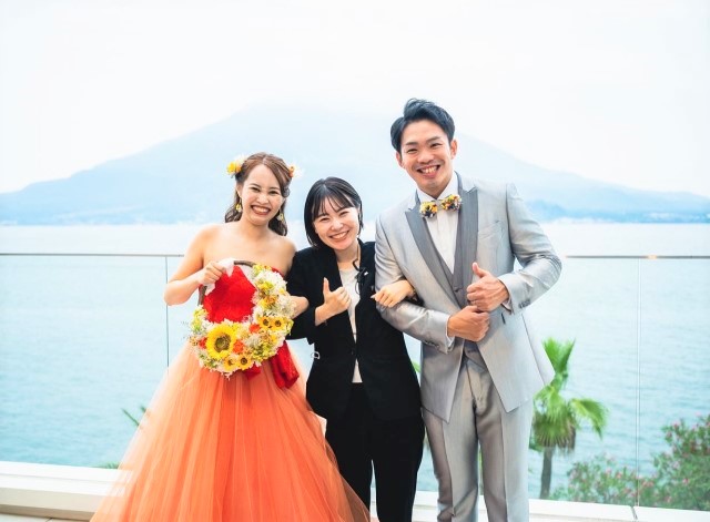 海辺のテラスで写真を撮る新郎新婦と式場スタッフ