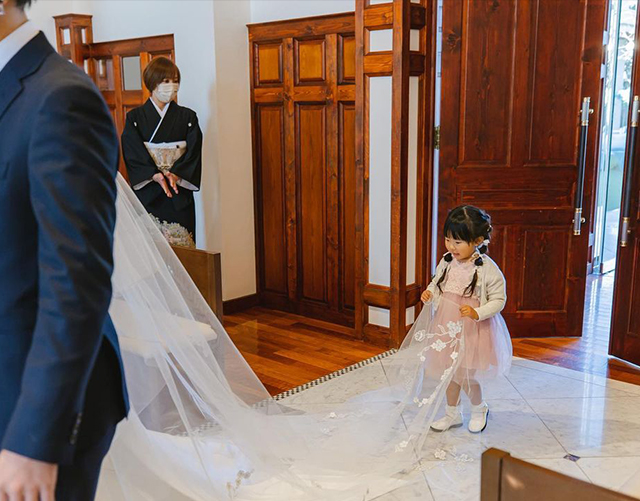 サイドで編みこみヘアをした花嫁のベールをもって歩く女の子