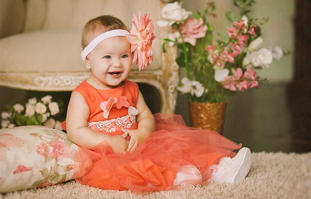 オレンジのベビードレスと大きな花の髪飾りを付けた赤ちゃん