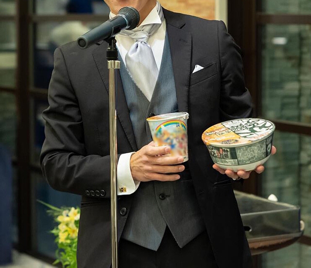 グレーのベストを着てスピーチをする男性