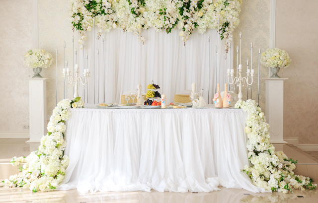 白い花をテーブルの両サイドから流れるように飾った高砂装花